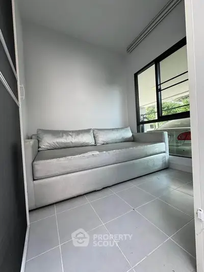 Modern small living room with sleek silver sofa and large window offering natural light.