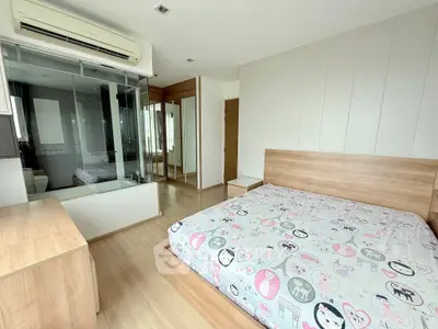 Spacious bedroom with modern decor and glass-enclosed bathroom, featuring wooden furniture and ample natural light.