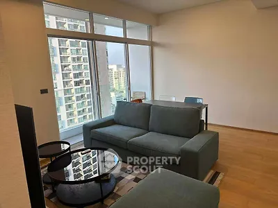 Modern living room with large windows and city view, featuring stylish furniture and wooden flooring.