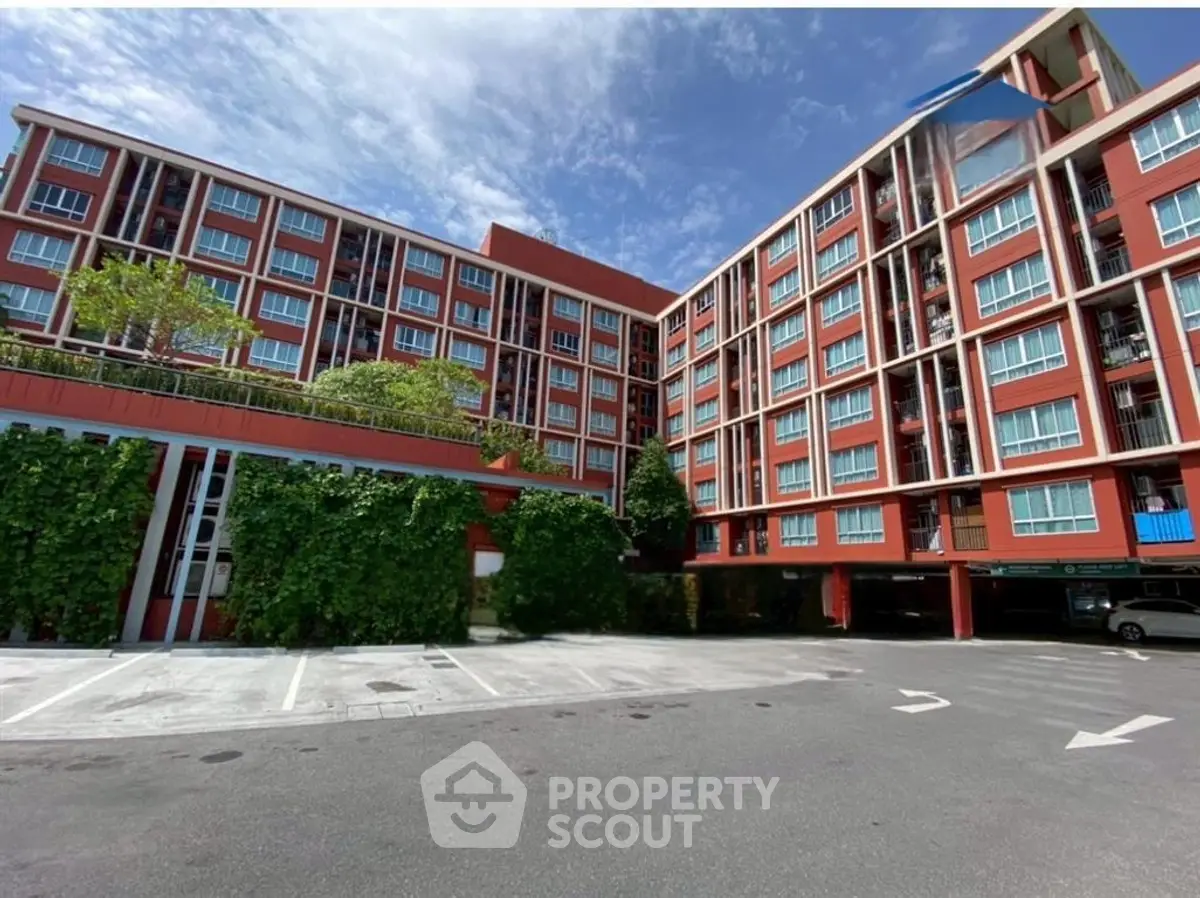 Modern red brick apartment building with lush greenery and spacious parking area.