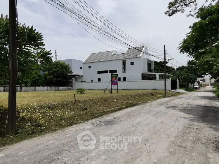 Modern white house with spacious yard and surrounding greenery on a quiet street.