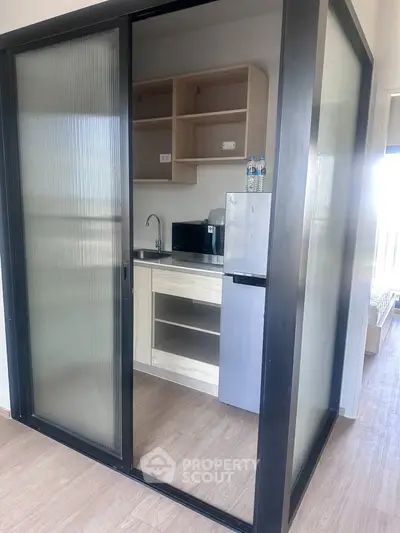 Modern compact kitchen with sliding glass doors and wooden cabinetry in a stylish apartment.