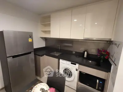 Modern kitchen with sleek cabinets, stainless steel fridge, washing machine, and microwave in compact layout.