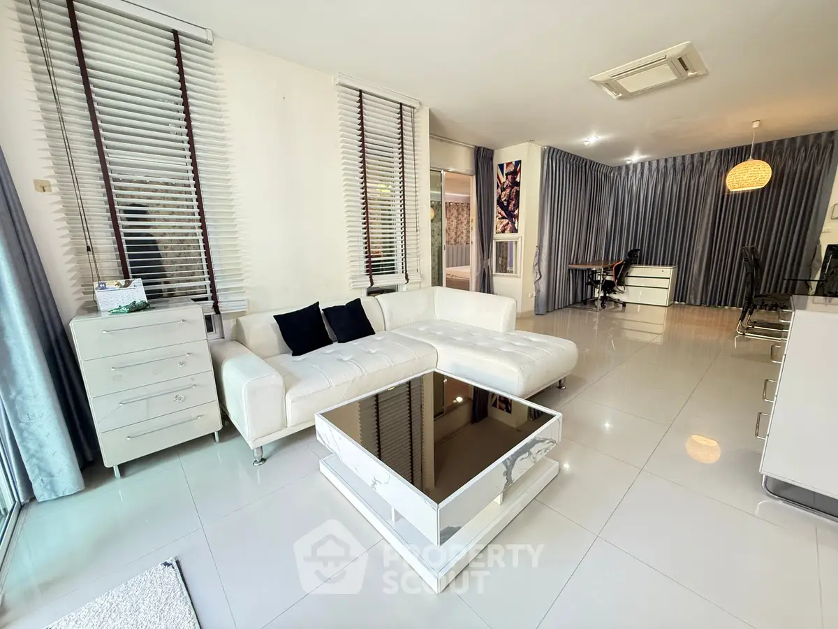 Spacious modern living room with sleek white furniture and large windows.