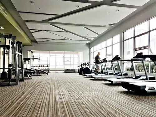 Spacious gym with modern equipment and large windows in a residential building.