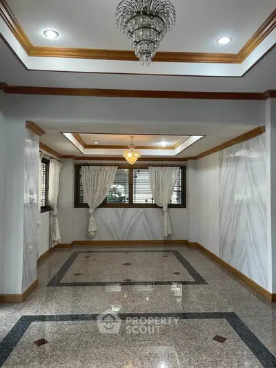 Elegant living room with marble flooring and chandelier, featuring large windows and classic curtains.
