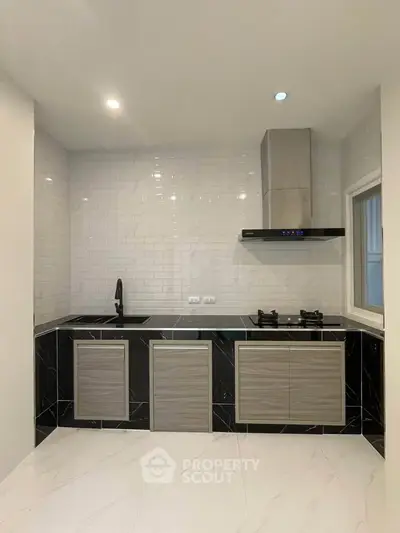 Modern kitchen with sleek black and gray cabinetry, gas stove, and stylish backsplash.