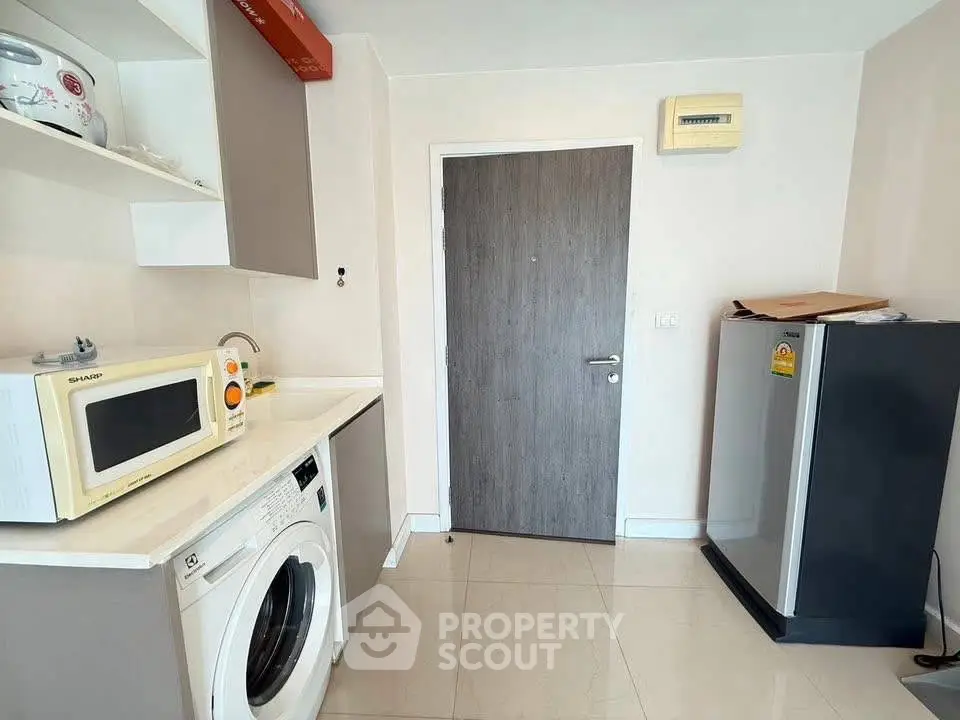 Modern kitchen with washing machine, microwave, and fridge in compact layout.