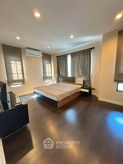 Spacious modern bedroom with wooden flooring and ample natural light.