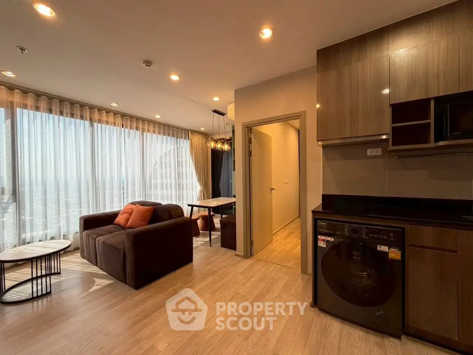Spacious modern living room with large windows and integrated kitchen featuring sleek appliances.