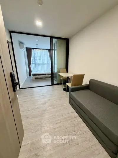 Modern studio apartment with sleek design and glass partition, featuring a cozy living area and bedroom.