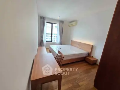 Spacious bedroom with wooden furniture and large window offering natural light.