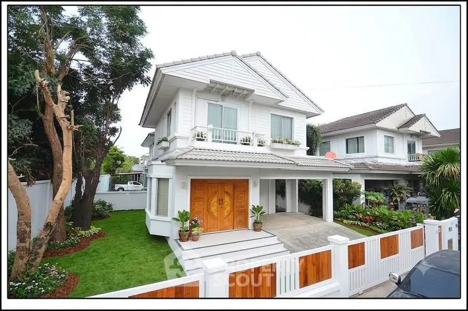 Charming two-story white house with lush garden and elegant wooden gate in a serene neighborhood.