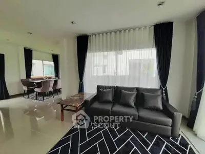 Spacious modern living room with elegant black sofa and dining area, featuring large windows and stylish decor.