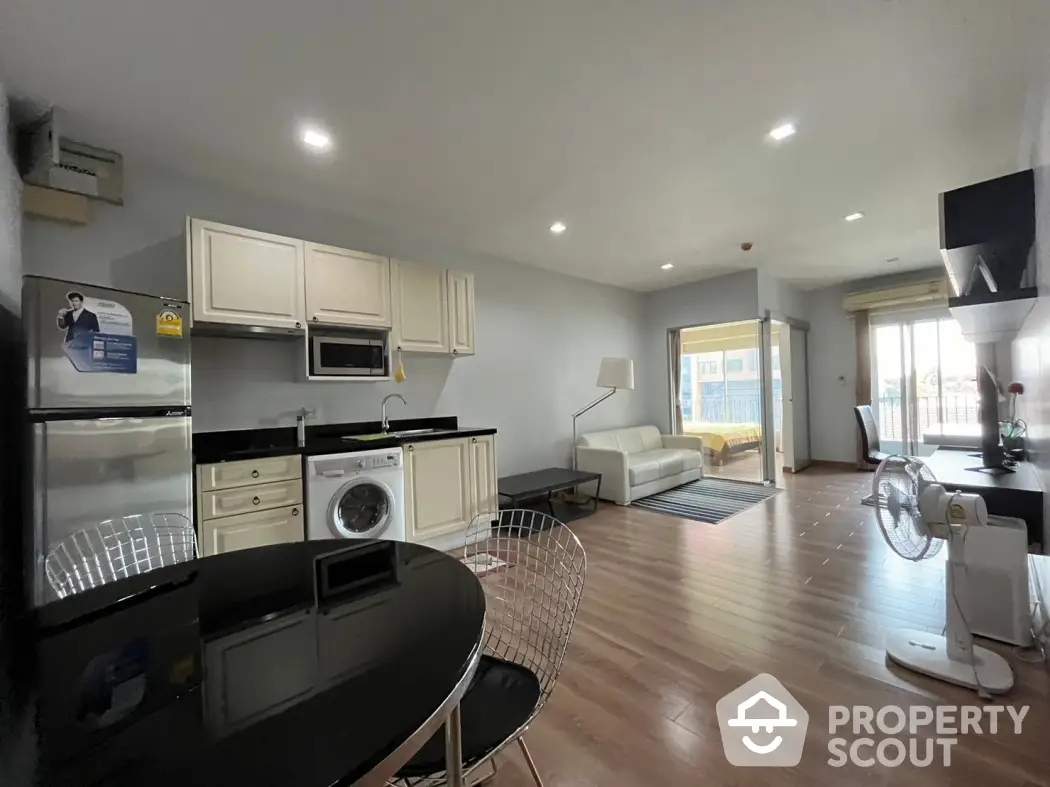 Modern open-plan living room with kitchen, featuring sleek furniture and balcony access.