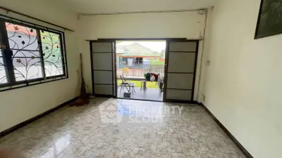 Spacious living room with sliding doors opening to a garden view, featuring tiled flooring and decorative window grills.