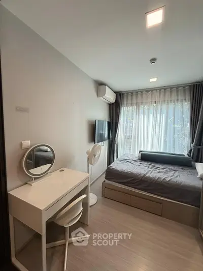 Modern bedroom with natural light, featuring a cozy bed, desk, and wall-mounted TV, ideal for urban living.