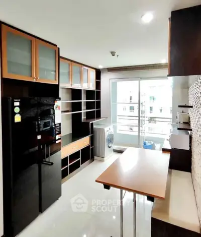 Modern kitchen with sleek cabinetry and appliances, featuring a washing machine and balcony access.
