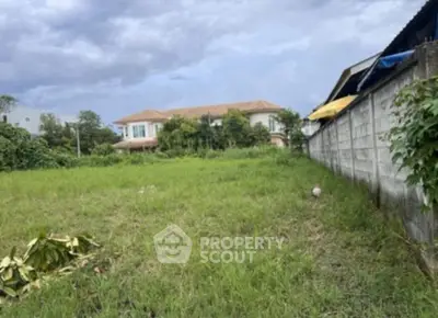 Spacious green plot of land with potential for development, surrounded by lush greenery and residential buildings.