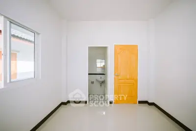 Minimalist interior with white walls and bright wooden door leading to a compact bathroom.