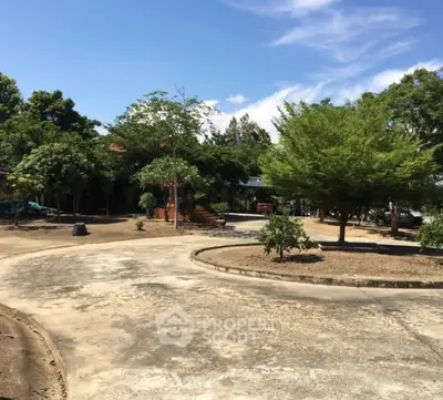 Spacious outdoor area with lush greenery and paved pathways under a clear blue sky.