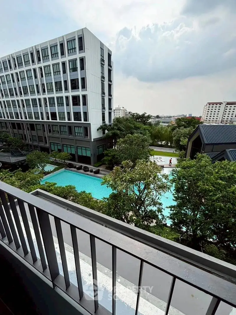 Modern apartment building with pool view from balcony, lush greenery surrounds the area.