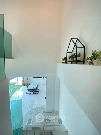 Elegant modern staircase with glass railing leading to a spacious living area with stylish decor.