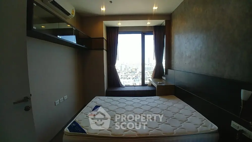 Modern bedroom with city view and large window, featuring a comfortable mattress and stylish decor.