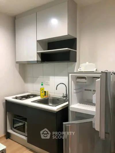 Modern compact kitchen with sleek cabinetry and open fridge in a stylish apartment.