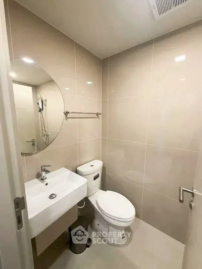 Modern bathroom with sleek fixtures and neutral tiles, featuring a round mirror and compact design.