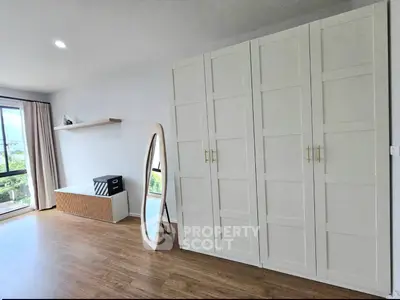 Spacious bedroom with large wardrobe and full-length mirror, featuring wooden flooring and natural light.
