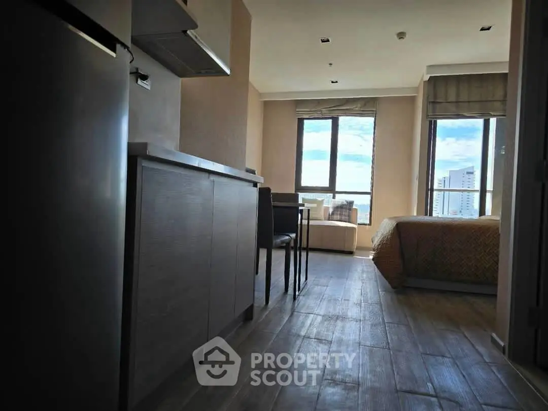 Modern apartment interior with open layout, featuring kitchen and living area with large windows and city view.
