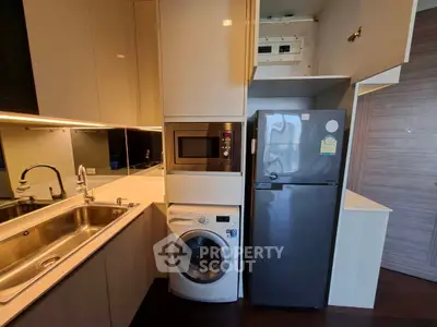 Modern kitchen with sleek appliances including fridge, microwave, and washing machine in compact layout.