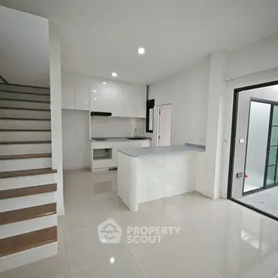 Modern open-plan kitchen with sleek white cabinetry and adjacent staircase