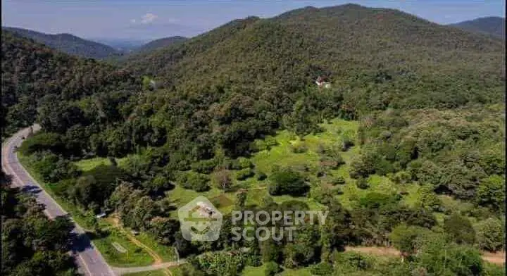 Scenic aerial view of lush green landscape with rolling hills and winding road, perfect for real estate development.