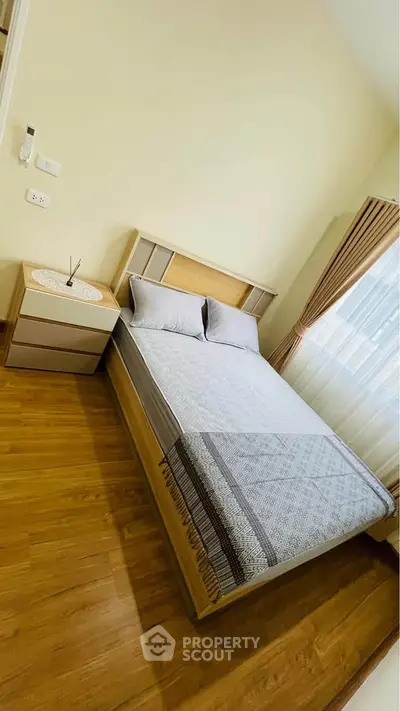 Cozy bedroom with wooden flooring and natural light, featuring a stylish bed and elegant curtains.