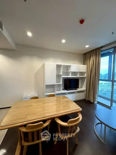 Modern dining area with wooden table and chairs, built-in TV unit, and city view from large window.