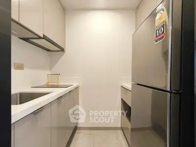 Modern kitchen with sleek cabinets and stainless steel fridge in compact layout.