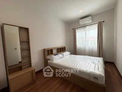 Cozy bedroom with wooden flooring, modern bed, and natural light from large window.