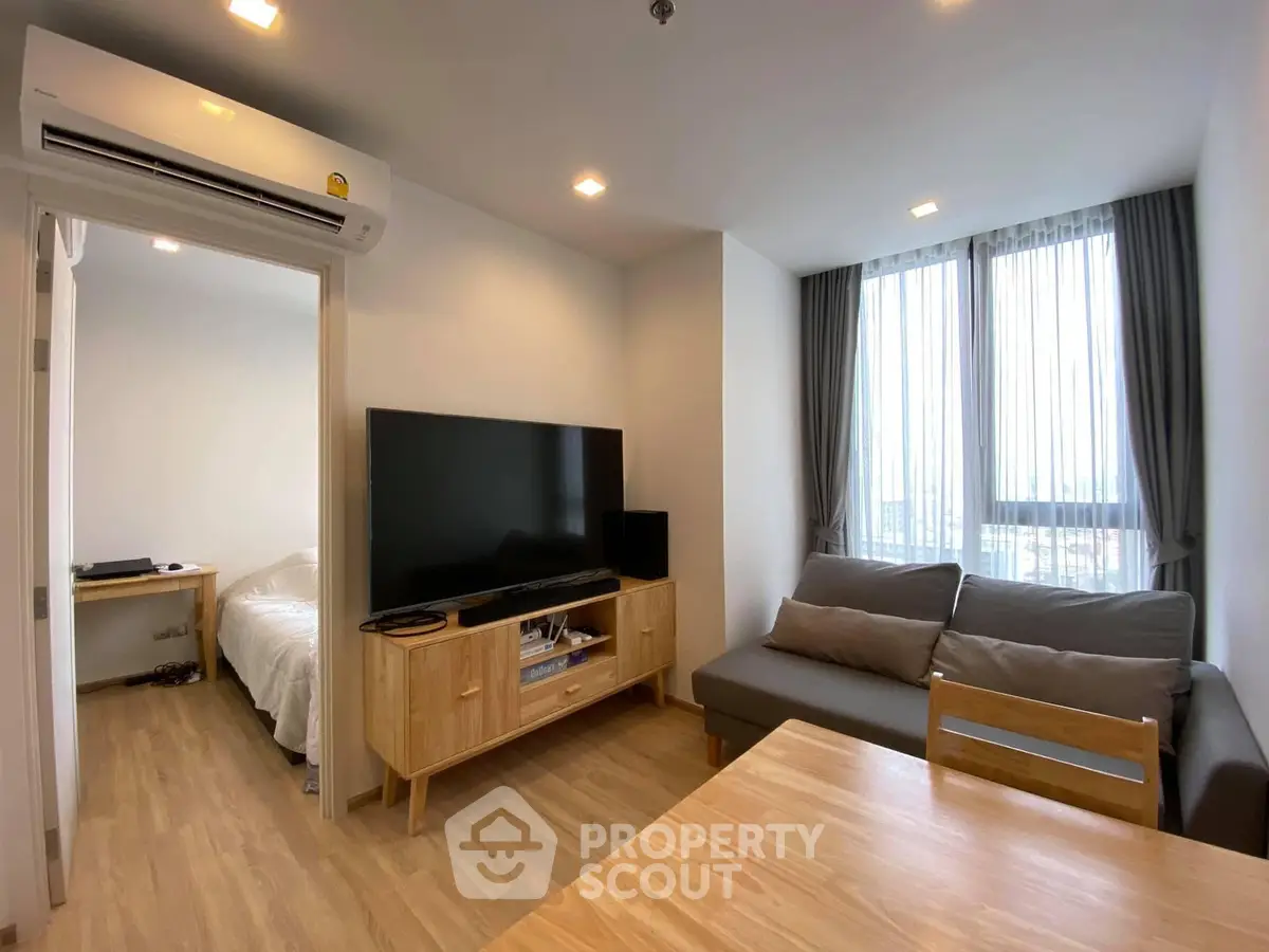Modern living room with wooden furniture and large TV, adjacent to cozy bedroom.