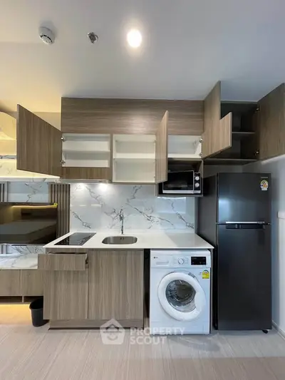 Modern kitchen with sleek cabinets, washing machine, and fridge in compact layout.