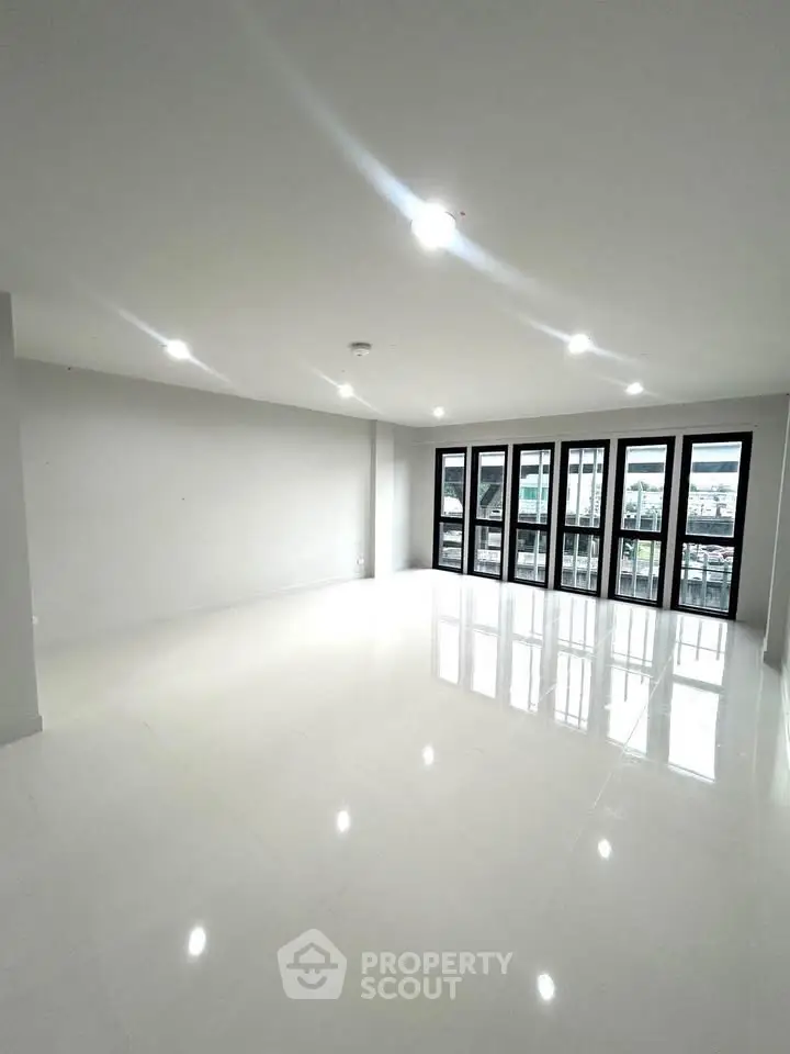 Spacious modern living room with large windows and glossy white flooring, offering ample natural light.