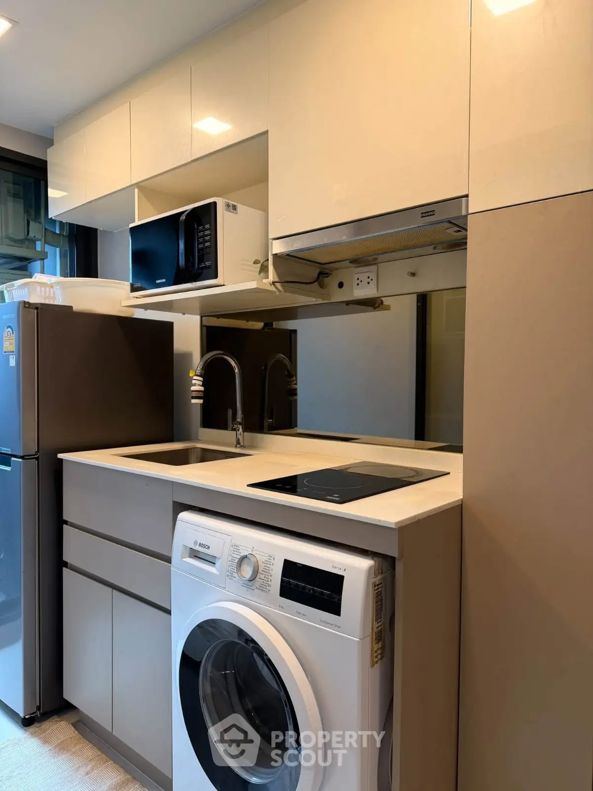 Modern compact kitchen with washing machine and microwave in sleek cabinetry.