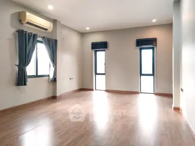 Spacious empty room with wooden flooring and large windows, perfect for customization.