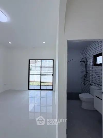 Modern interior with bright living space and adjacent bathroom, featuring sleek tiles and large windows.
