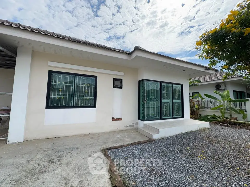 Charming single-story home with large windows and a gravel yard under a picturesque sky.