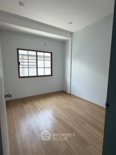 Spacious empty room with wooden flooring and large window, perfect for customization.