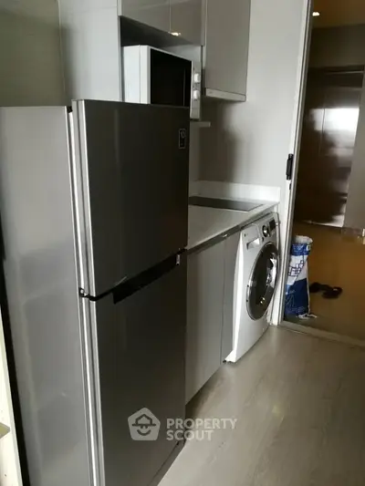 Modern kitchen with sleek appliances including fridge and washing machine in compact layout.
