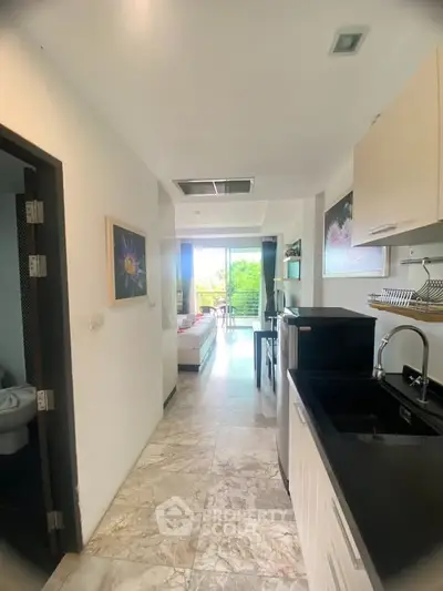 Modern open-layout apartment with sleek kitchen and bright living area leading to a balcony with lush views.