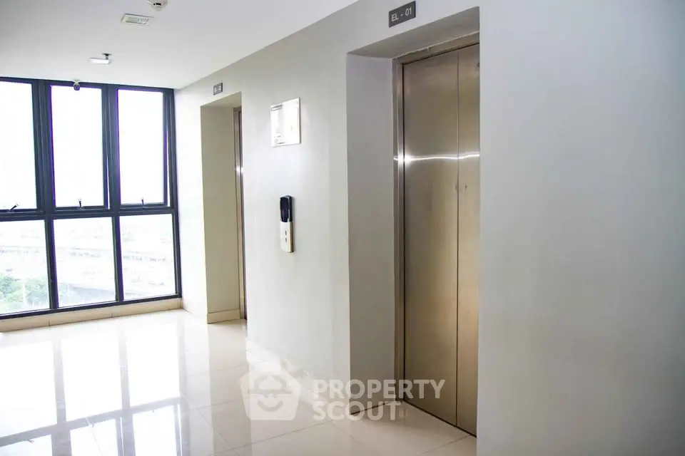 Modern building corridor with elevators and large windows offering natural light.